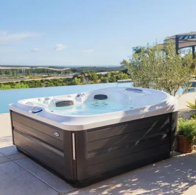 Large dark-cabinet hot tub with bubbling jets on a stone patio overlooking a scenic landscape