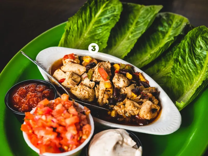 Green plate with chicken and black bean filling, romaine lettuce wraps, pico de gallo, salsa, and sour cream