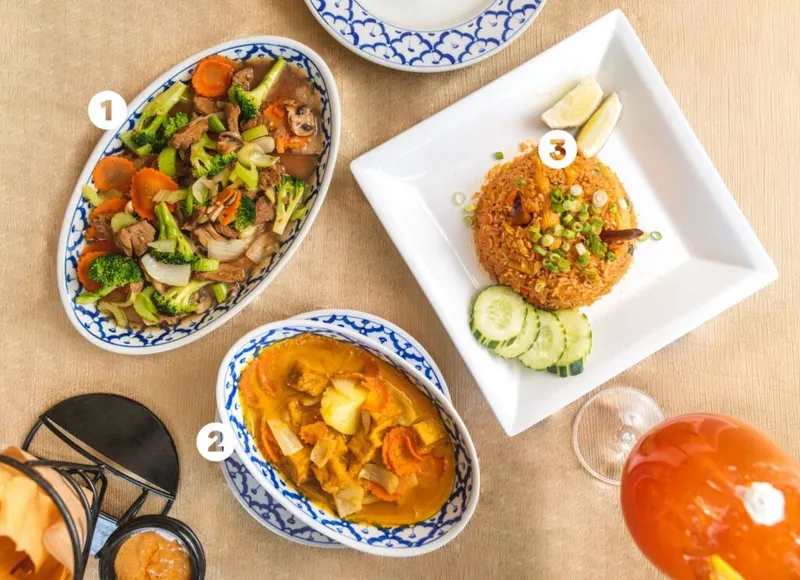 Overhead spread of three numbered Thai dishes: stir-fried vegetables, yellow curry, and fried rice with cucumber slices