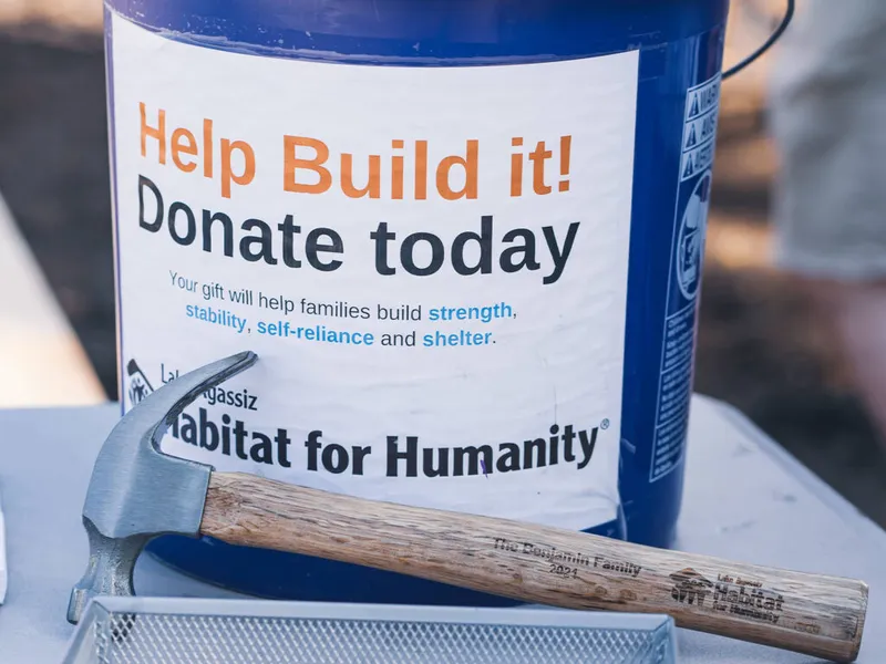 Habitat for Humanity donation bucket beside an engraved wooden-handled hammer
