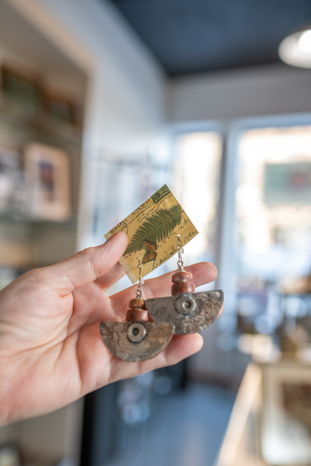 Hand holding a pair of rustic half-moon earrings on a fern-printed card