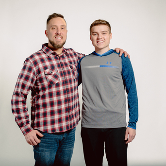 Two smiling men stand together, one with arm around the other's shoulder