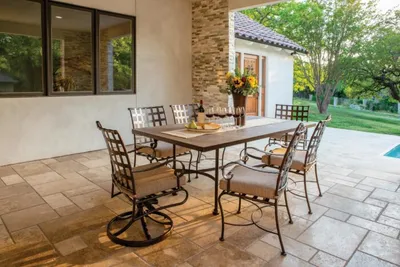 Wrought-iron patio dining set with six cushioned chairs on a stone tile patio