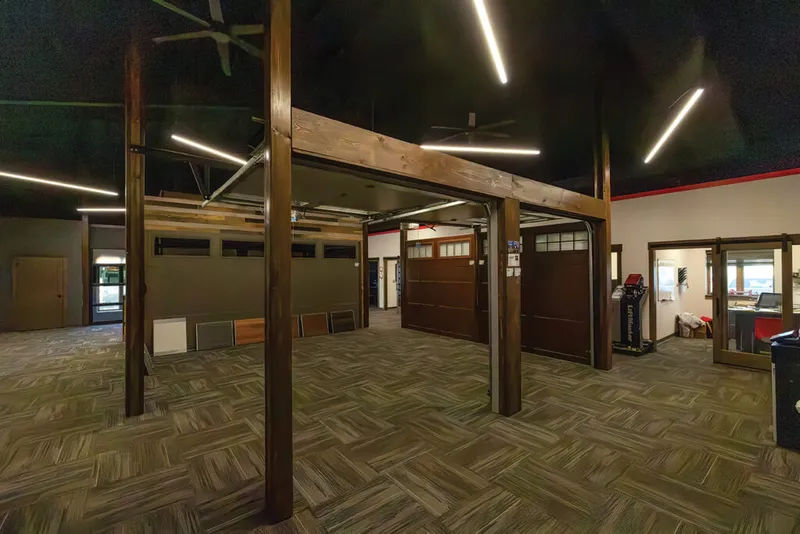 Showroom interior with wood-beam framework displaying garage door samples under a dark ceiling with linear LED lighting