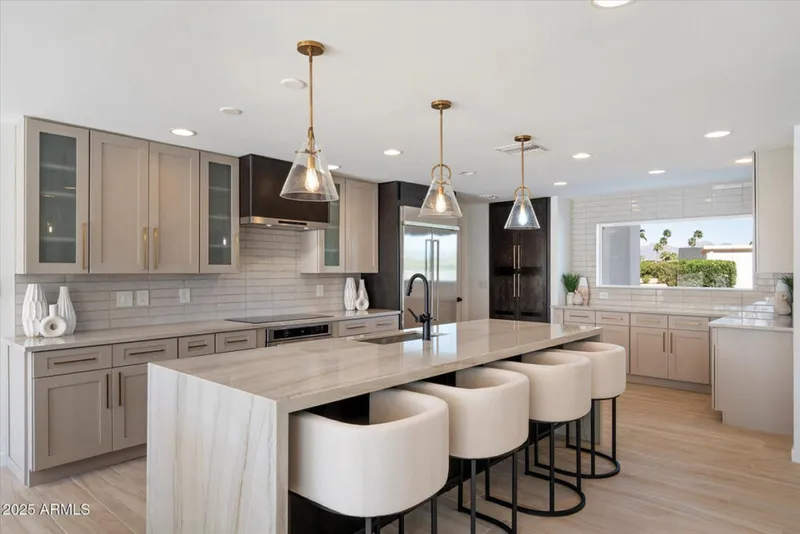 Modern kitchen with marble island, cream bar stools, and brass pendant lights over light wood floors