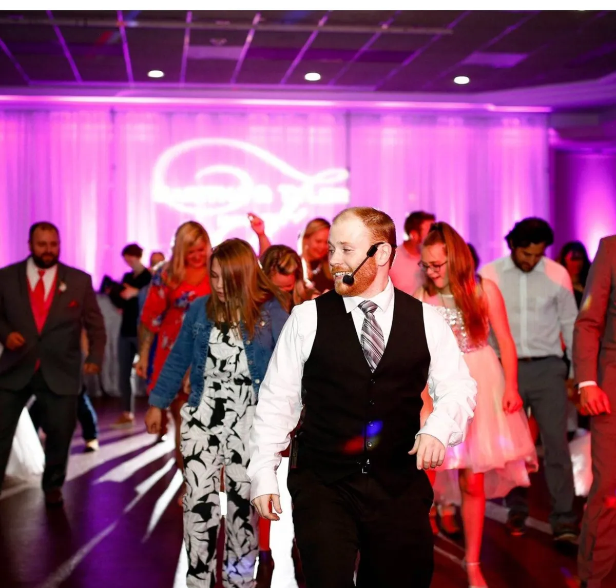 Bearded emcee with headset mic leads a crowd dancing under purple event lighting