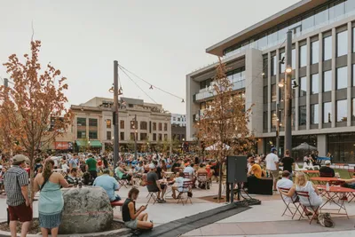 Crowd of people gathered in an outdoor urban plaza surrounded by modern buildings at dusk