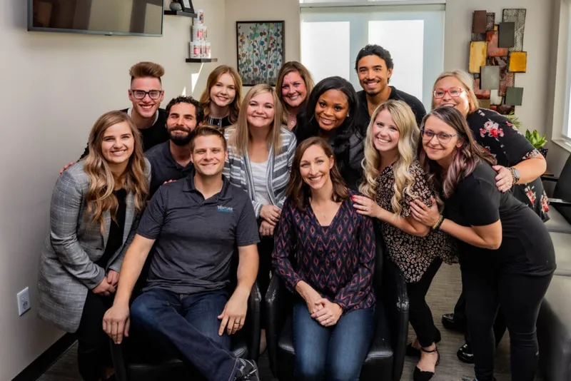 Group of about twelve smiling people posing together inside an office or salon