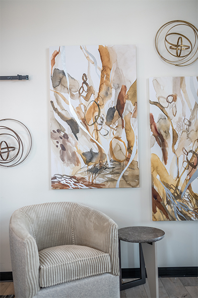 Striped barrel chair beside abstract earth-tone paintings and gold orbital wall sculptures