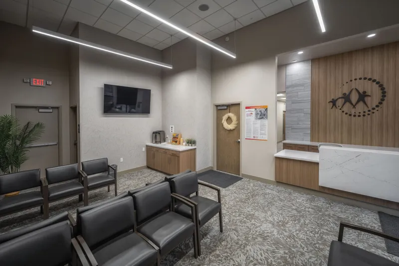 Modern medical waiting room with dark leather chairs, wall-mounted TV, and a reception desk with wood paneling