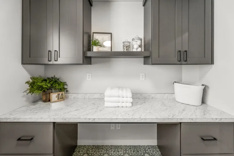Laundry room with gray shaker cabinets, marble countertop, folded white towels, and a floating shelf
