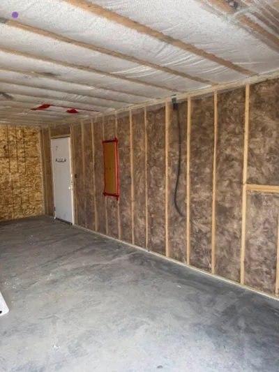 Unfinished room interior with exposed wood studs and batt insulation on walls and ceiling