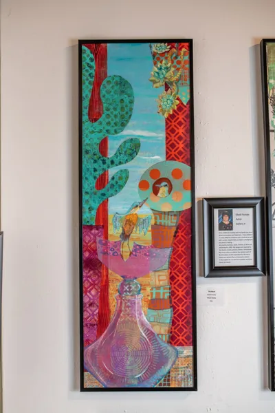Tall framed mixed-media painting with colorful cacti, patterned panels, and figurative elements hanging on a gallery wall