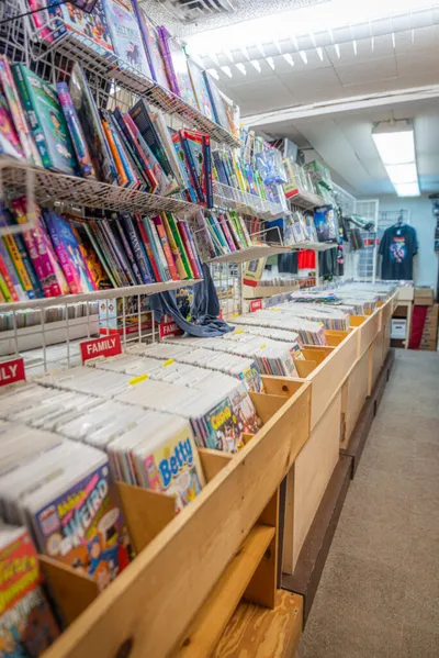Comic book store interior with long bins of bagged comics and shelves of graphic novels lining the walls