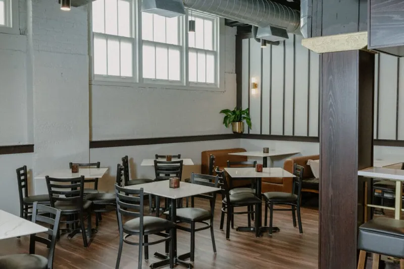 Bright restaurant dining room with black chairs, white marble tables, and leather booth seating