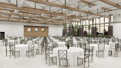 Spacious event hall with round white-draped tables, metal chairs, and large windows