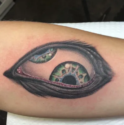 Detailed color tattoo of a rolling green eye on a forearm