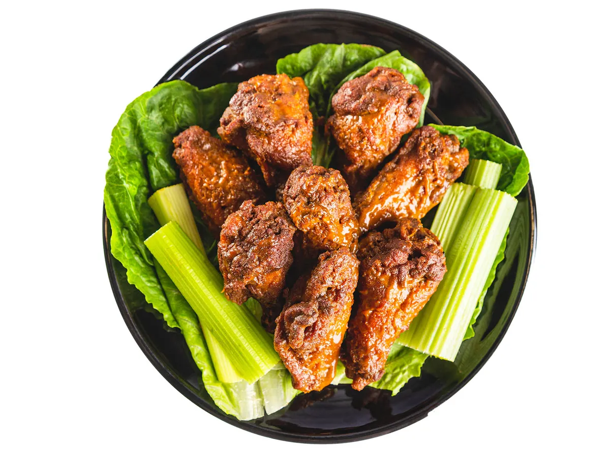 Saucy chicken wings on a dark plate lined with lettuce and celery sticks