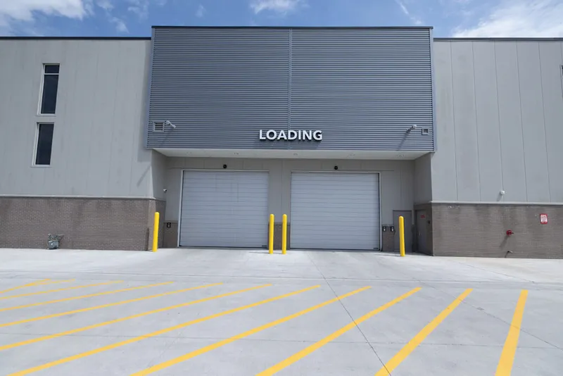 Loading dock with two white roll-up doors, yellow bollards, and striped concrete apron