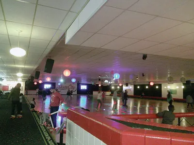Indoor roller skating rink with colorful overhead lights and skaters on the floor