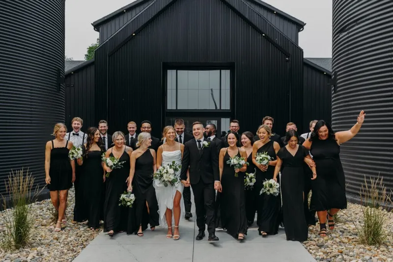 Wedding party in all-black attire walking in front of a black metal barn venue