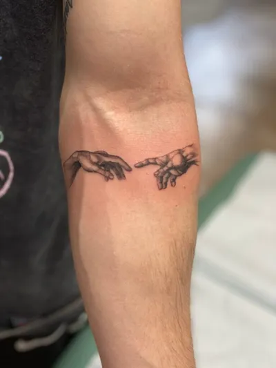 Black and grey tattoo of two reaching hands on a forearm
