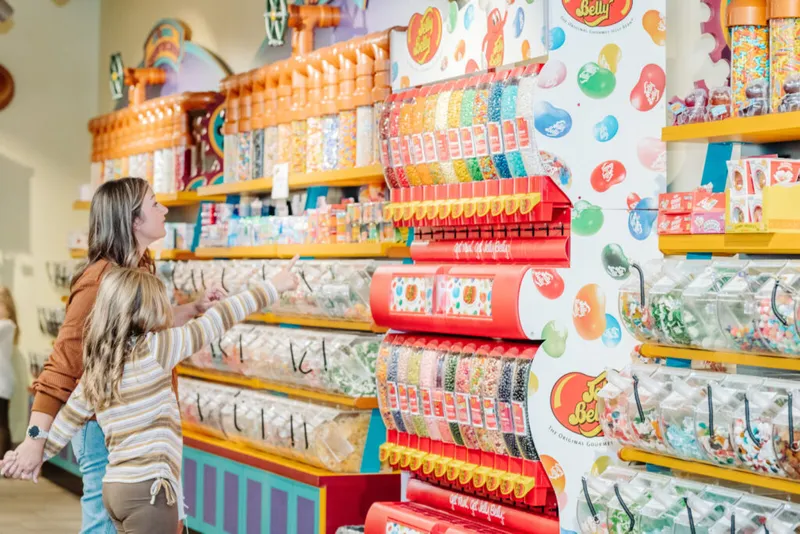 Woman and child browsing a colorful Jelly Belly candy display wall in a store