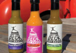 Three hot sauce bottles with colorful labels on a blue surface