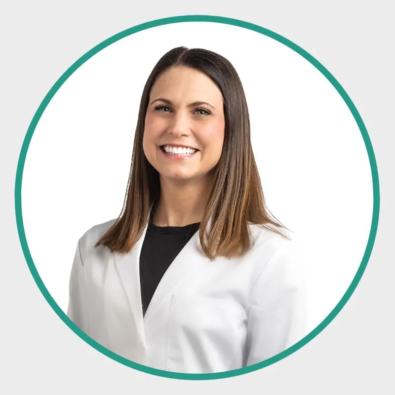 Smiling woman with long brown hair wearing a white medical coat