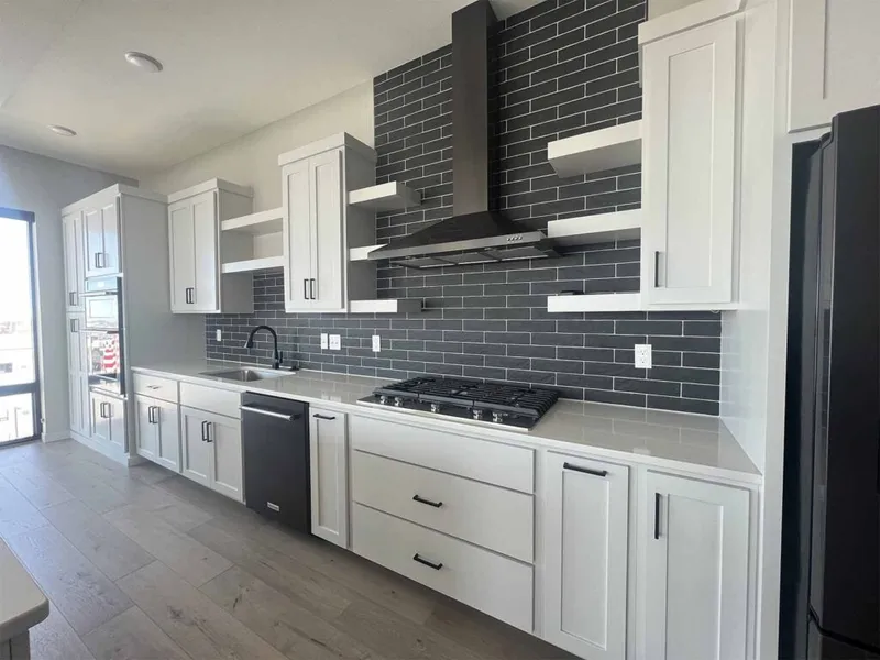 Modern kitchen with white shaker cabinets, dark subway tile backsplash, and black range hood