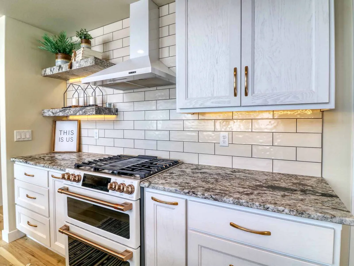 Renovated kitchen with white cabinets, gold hardware, subway tile backsplash, and a white gas range with copper accents