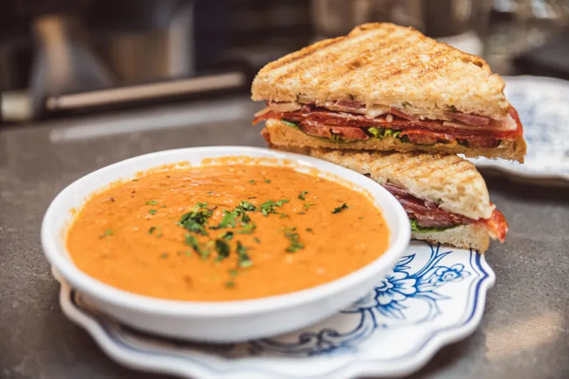 Tomato soup with herb garnish beside a halved grilled meat panini on a blue-and-white plate