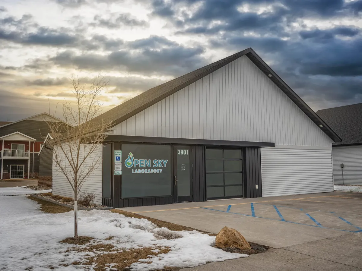 Open Sky Laboratory exterior at 3901, white barn-style building with snowy parking lot under dramatic cloudy sky