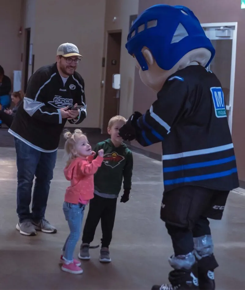 Two young children greet a hockey mascot in a blue helmet while a man in a hockey jersey looks on