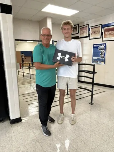 Older man and young man jointly holding a dark Under Armour shoebox in a school hallway