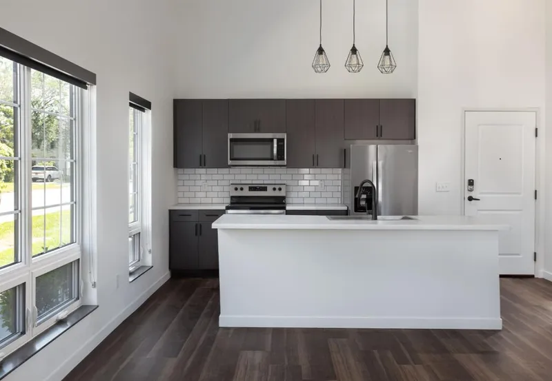 Modern kitchen with dark cabinets, white island, subway tile backsplash, and three geometric pendant lights