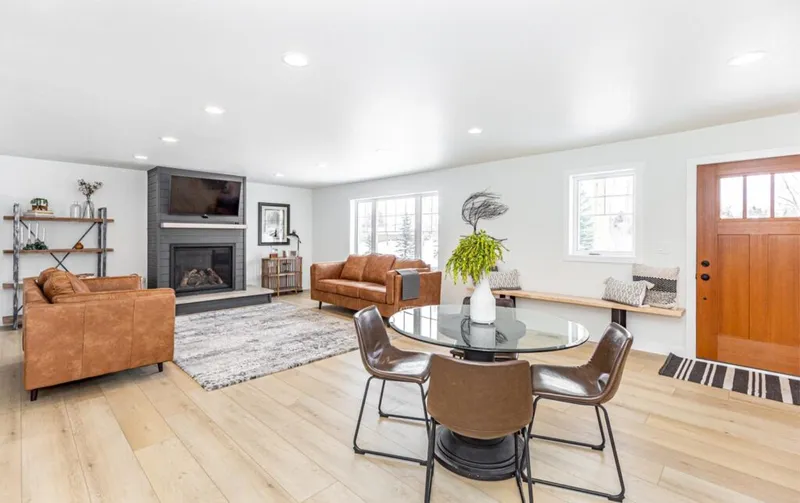 Open-concept living and dining area with tan leather sofas, gray stone fireplace, and round glass dining table