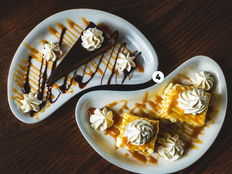 Two white plates with chocolate cake slice and yellow dessert bars drizzled with caramel and chocolate, topped with whipped