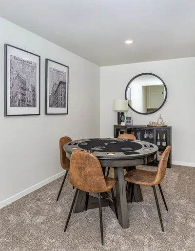 Round poker table with tan leather chairs in a carpeted game room with framed prints and a round mirror