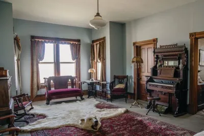 Victorian parlor with ornate wooden organ, velvet settee, and animal-skin rug