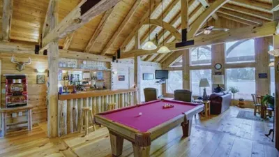 Red felt pool table in a log cabin great room with vaulted wood-beam ceiling and bar area
