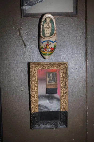 Decorative wooden clog and ornate gold-framed mirror mounted on a dark wall