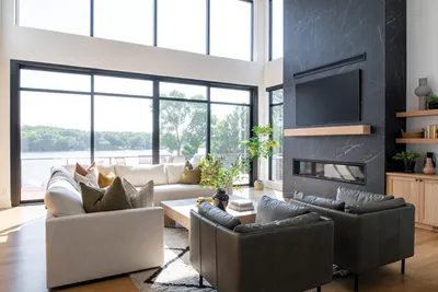 Modern living room with dark stone fireplace, white sectional, and floor-to-ceiling windows overlooking a lake