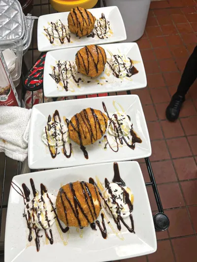 Four white plates each holding a fried dough ball with ice cream drizzled in chocolate sauce