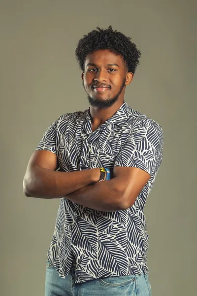 Young man with curly hair and beard, arms crossed, wearing a leaf-print shirt