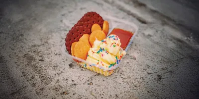 Ice cream with rainbow sprinkles and red waffle cookies in a small plastic tray