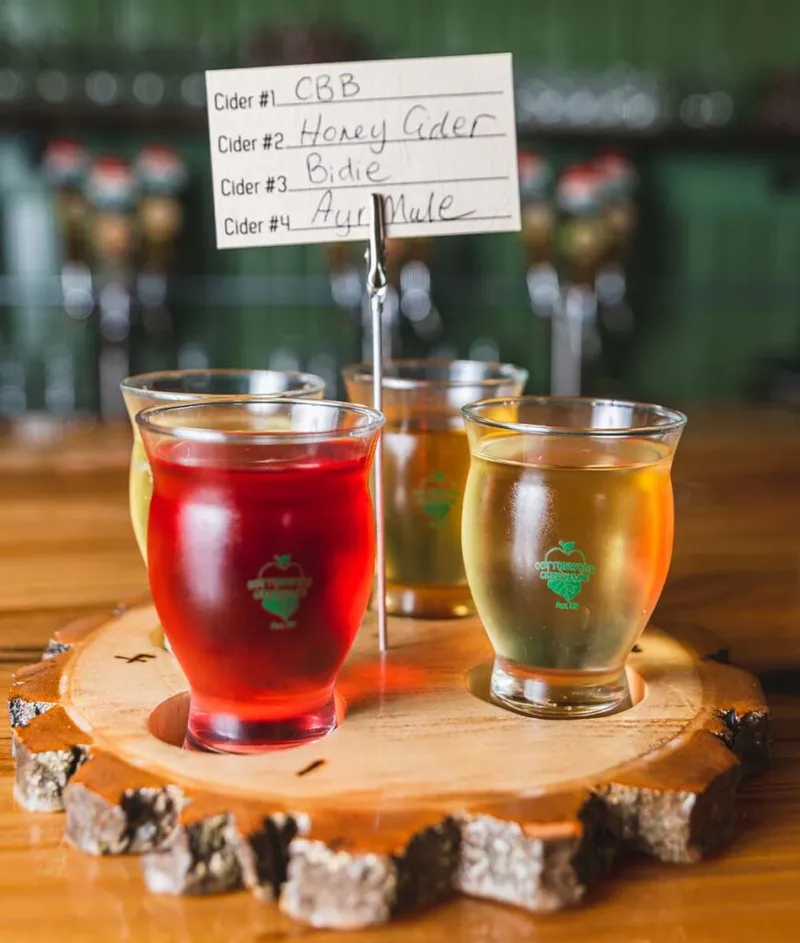 Four cider tasting glasses on a wood slice board with a handwritten flavor menu card