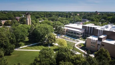 Aerial view of a college campus with a bell tower, green lawns, and modern buildings amid trees