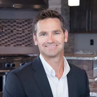 Smiling man in dark blazer and white shirt standing in a modern kitchen