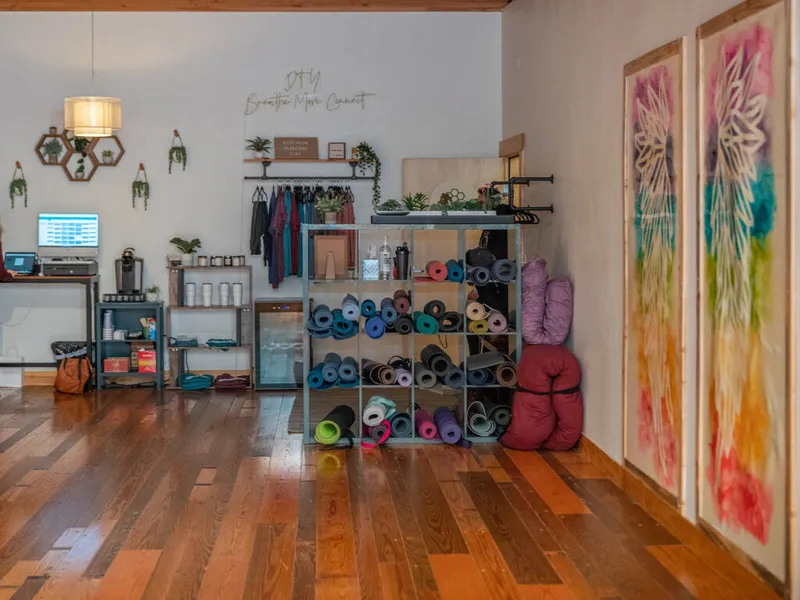 Bright yoga studio interior with rolled mats on shelving, hanging clothes, wood floors, and colorful wall art